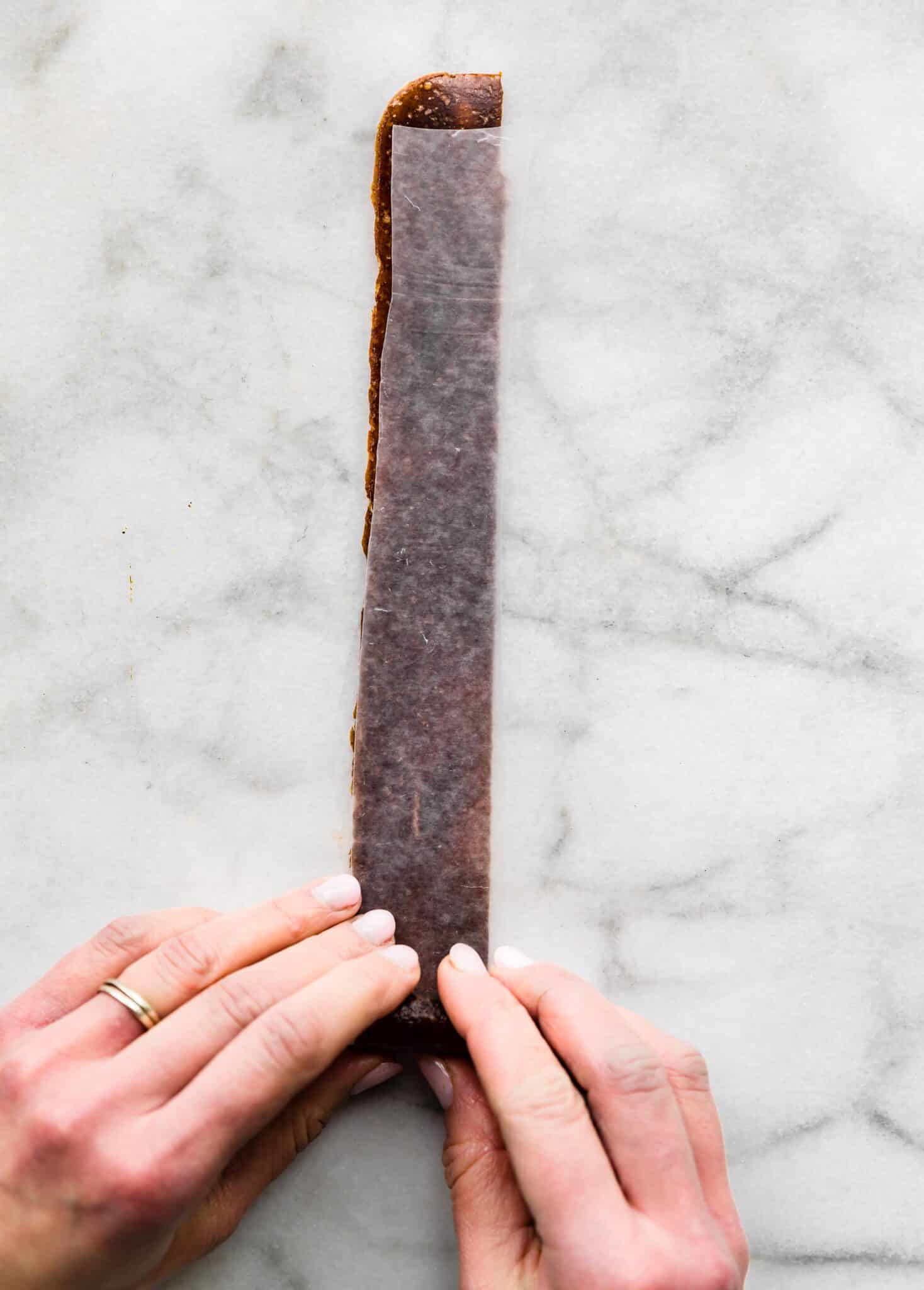 A woman's hands rolling up a homemade fruit roll up on strips of parchment paper.