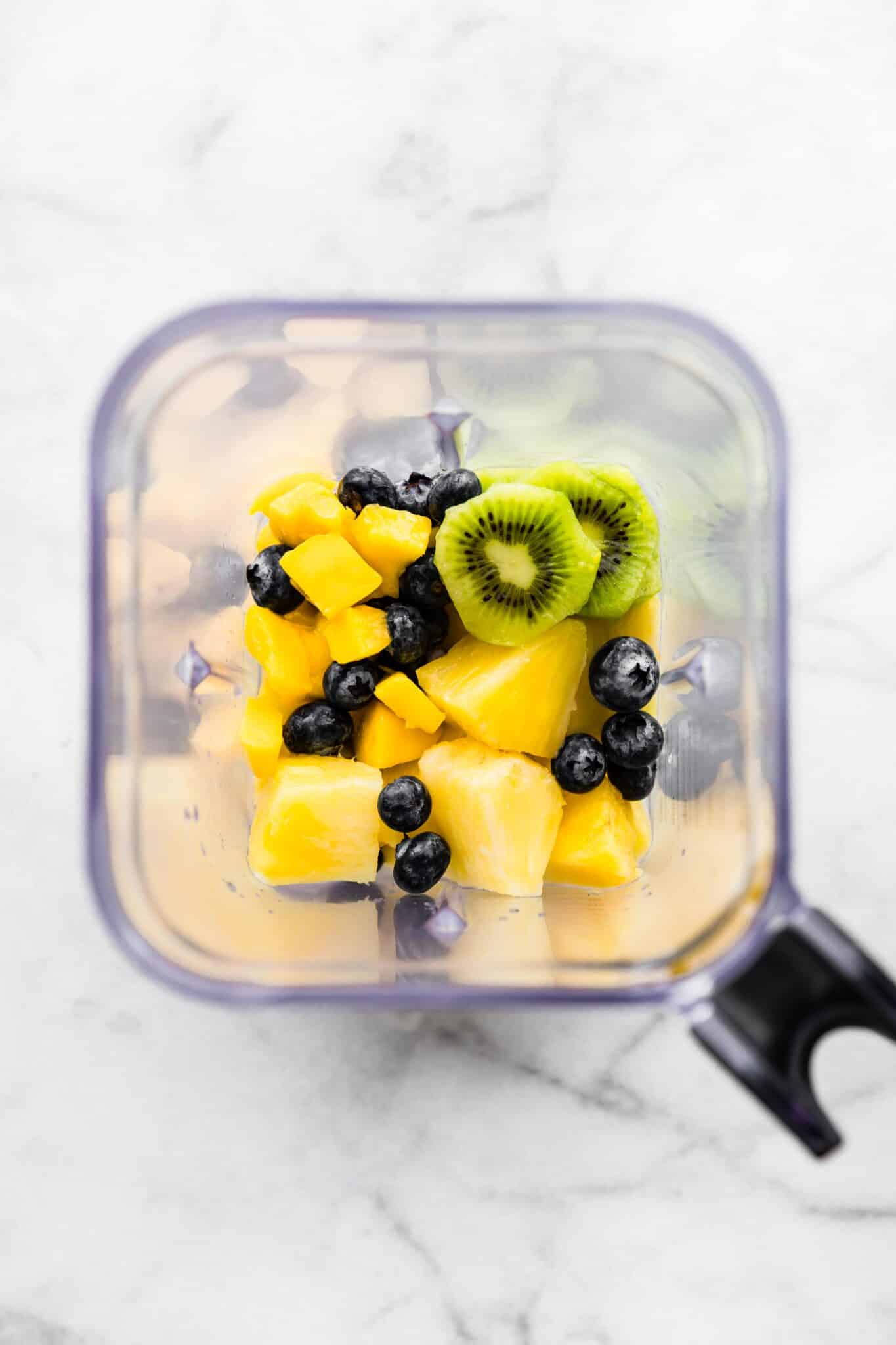 Overhead photo of pineapple chunks, kiwi slices and blueberries in a blender.