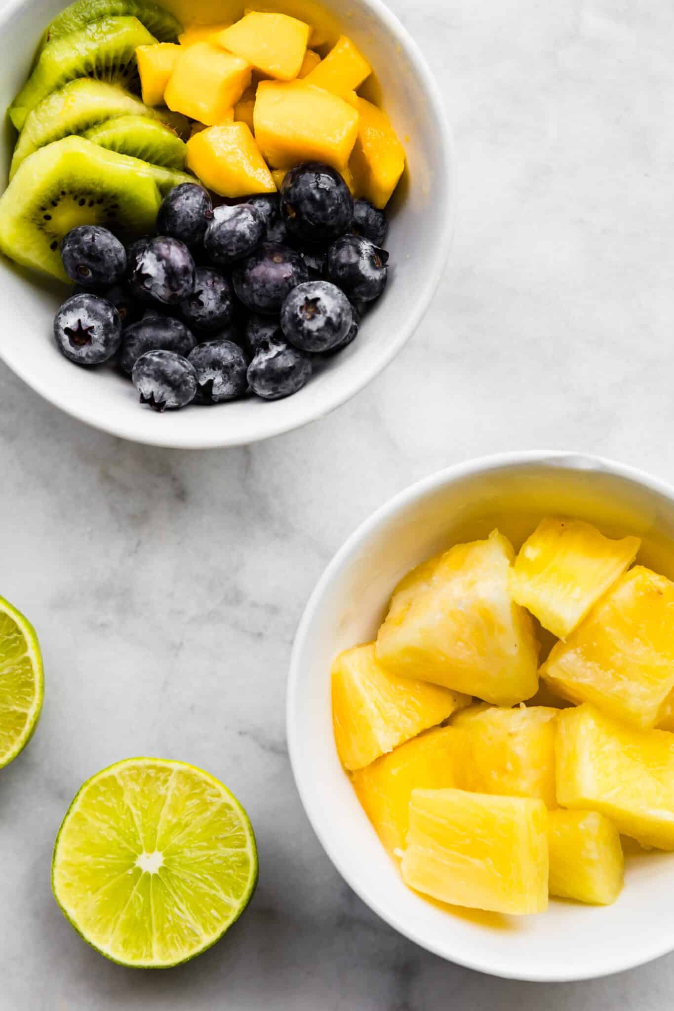 Overhead photo of bowls of pineapple chunks, blueberries and kiwi slices.