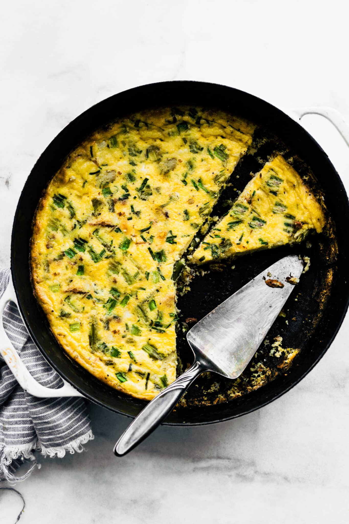 Baked vegetable frittata in a cast iron pan with serving utensil and a separated slice.